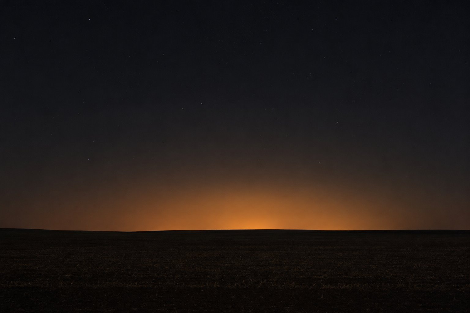 An orange skyglow dome beyond dark fields.